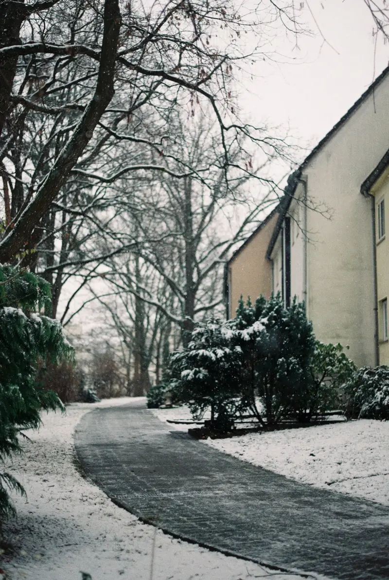 Geräumter Gehweg entlang eines Hauses, links und rechts liegt Schnee