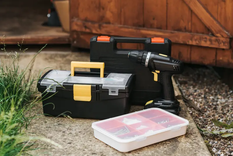 Werkzeugkoffer, Akkuschrauber und ein Schraubensortiment vor einer Holztür
